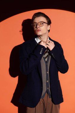 Genç adam, turuncu bir arka planda dururken modern gençlik modasını sergiliyor..