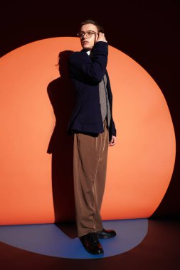 Moda elbiseli kendine güvenen genç, renkli bir arkaplan önünde tek eliyle poz veriyor..