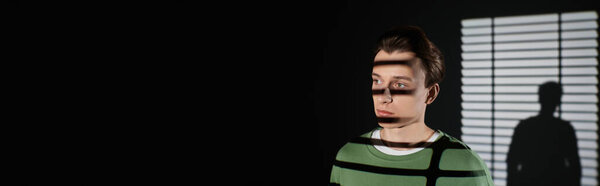 Young man displays a trendy outfit while shadows create an artistic contrast on the wall.