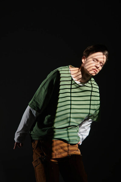 Модный подросток уверенно позирует, с тенями, добавляющими драмы в его стильный наряд.