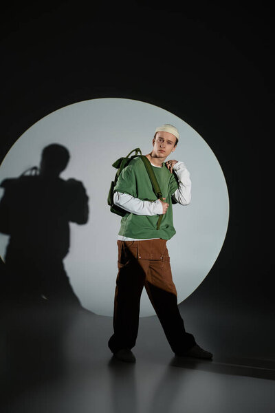 Модный подросток стоит с рюкзаком, демонстрируя современную молодежную моду и стиль.