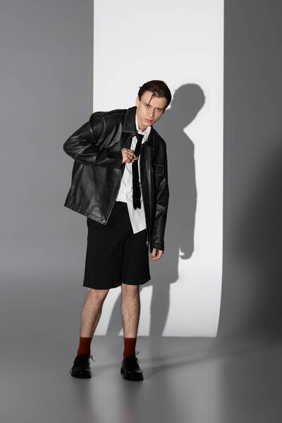 A fashionable teenager stands confidently, dressed in sleek attire, against a minimalist backdrop.