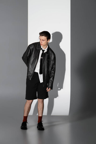 A confident teen in a leather jacket and shorts embodies youthful culture.