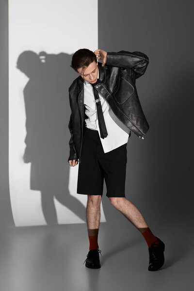 A stylish teenager interacts with his outfit while posing confidently against a minimalist backdrop.