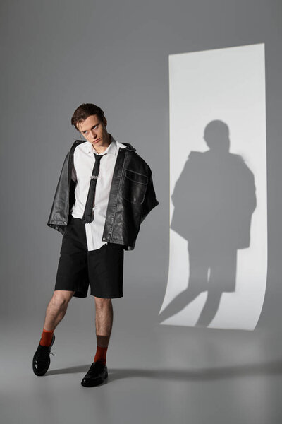 Young man dressed in trendy attire poses against a minimalist background, emanating confidence.