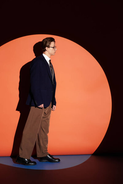 Молодой человек в индивидуальном костюме позирует на фоне большого круга в стильном помещении.