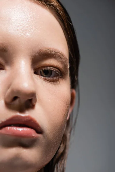 Обрізаний вид жінки з мокрою шкірою дивиться на камеру ізольовано на сірому — стокове фото