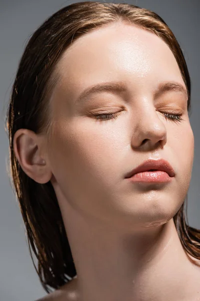 Ritratto di giovane donna con pelle bagnata che chiude gli occhi isolati su grigio — Foto stock
