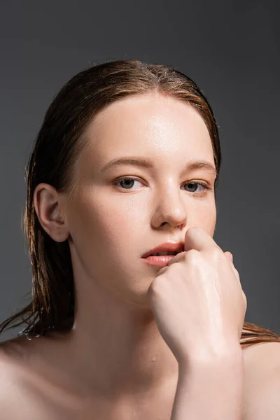 Молода жінка з мокрою шкірою і волоссям тримає руку біля обличчя ізольовано на сірому — стокове фото