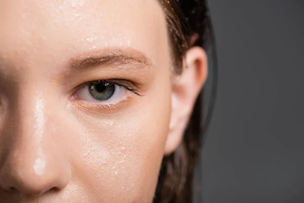 Обрізаний вид жінки з мокрою шкірою і розмитим волоссям дивиться на камеру ізольовано на сірому — стокове фото