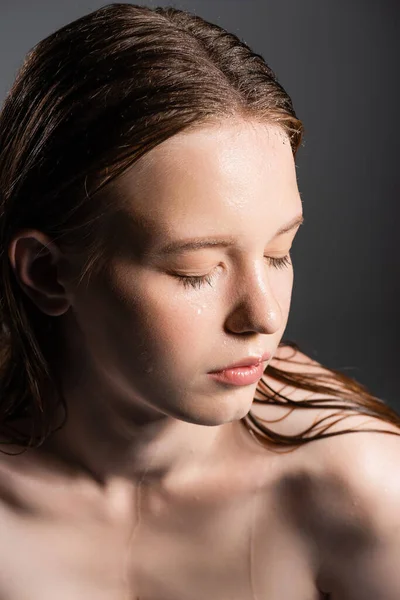 Modelo jovem com cabelo molhado e ombro nu fechando olhos isolados em cinza — Fotografia de Stock