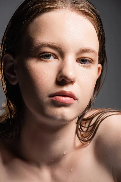 Modelo joven con cabello mojado y gotas de agua en el cuello mirando a la cámara aislada en gris - foto de stock