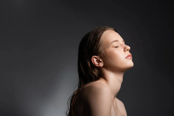 Красивая молодая женщина с каплями воды на лице позирует на сером фоне — стоковое фото