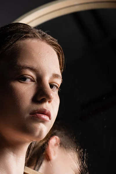 Junges Model mit nasser Haut im Gesicht blickt in Kamera in der Nähe von verschwommenem Spiegel — Stockfoto
