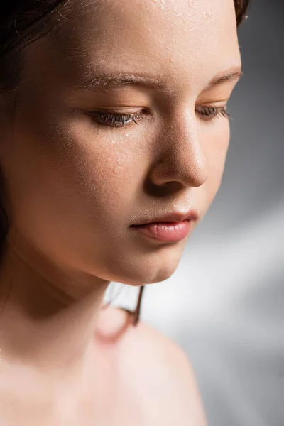 Молодая женщина с капельками воды на лице на абстрактном сером фоне — стоковое фото