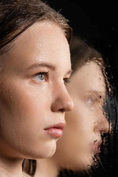 Close up view of fair haired woman with wet skin looking away near blurred mirror on black — Stock Photo