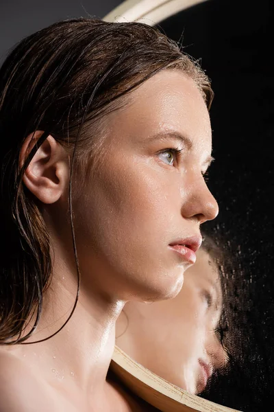 Schönhaariges Modell mit nassem Gesicht, das in der Nähe eines Spiegels auf grauem Hintergrund steht — Stockfoto