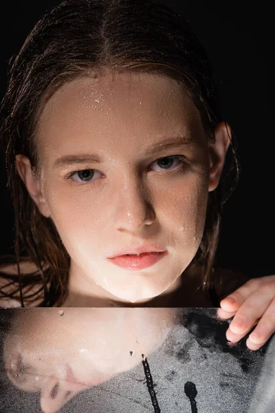 Портрет модели с влажным лицом, касающимся зеркала, изолированного на черном — стоковое фото