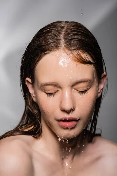 Portrait de jeune femme avec de l'eau sur la peau fermant les yeux sur fond gris — Photo de stock