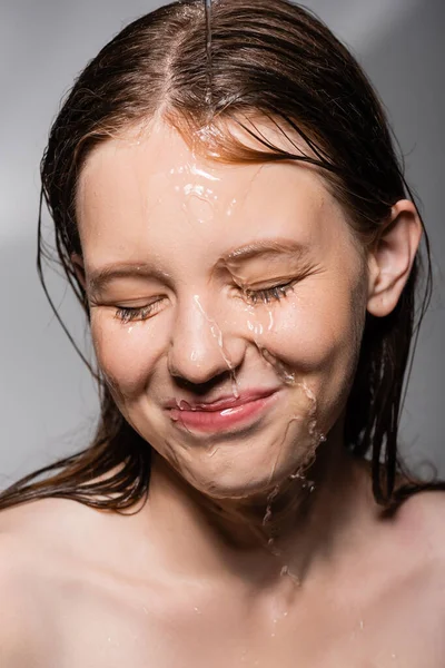 Усміхнена жінка з водою на обличчі закриває очі на сірому фоні — стокове фото