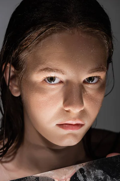 Ritratto di donna con pelle bagnata che guarda la macchina fotografica vicino allo specchio con luce isolata sul grigio — Foto stock