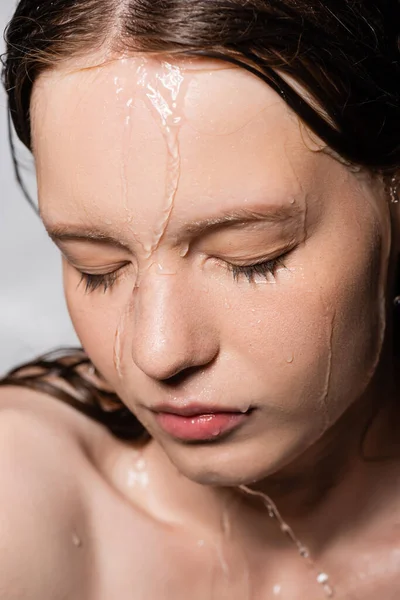Vue rapprochée de l'eau qui coule sur le visage d'une jeune femme isolée sur fond gris — Photo de stock