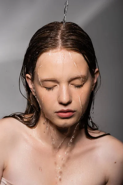 Water pouring on hair and face of young model on grey background — Stock Photo