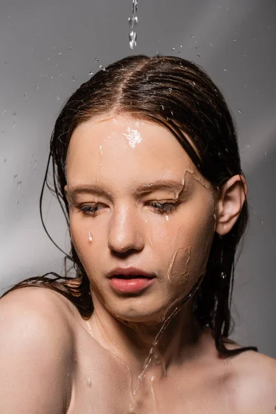 Junge Frau mit nackten Schultern steht unter Wasser und gießt auf grauem Hintergrund — Stockfoto