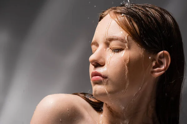 Hübsche junge Frau mit nackter Schulter steht unter Wasser auf abstraktem grauen Hintergrund — Stockfoto