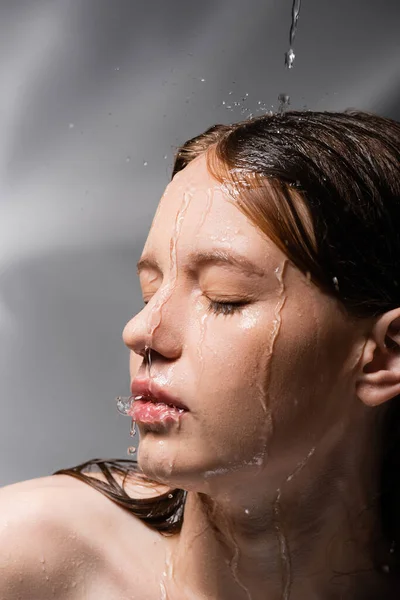 Молодая модель с водой на лице и волосах, стоящая на абстрактном сером фоне — стоковое фото