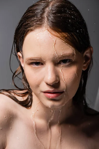 Портрет молодой женщины с водой на лице и волосах, смотрящей в камеру на сером фоне — стоковое фото