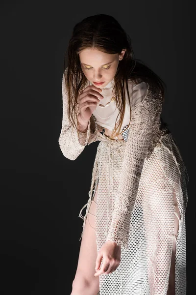 Stylish young model in fishnet skirt and knitted cardigan looking down isolated on black with light — Stock Photo