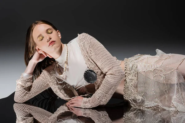 Mermaid in knitted cardigan and fishnet skirt lying on mirror on grey background — Stock Photo