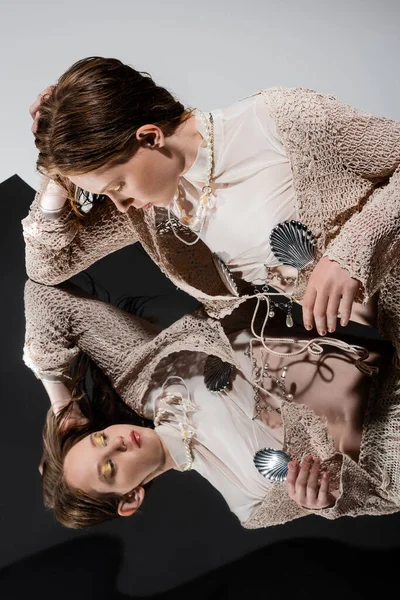 Sirène en cardigan tricoté et collier de perles regardant miroir sur fond gris — Photo de stock