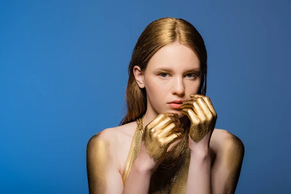 Portrait de femme aux cheveux blonds avec peinture dorée sur les mains isolées sur bleu — Photo de stock