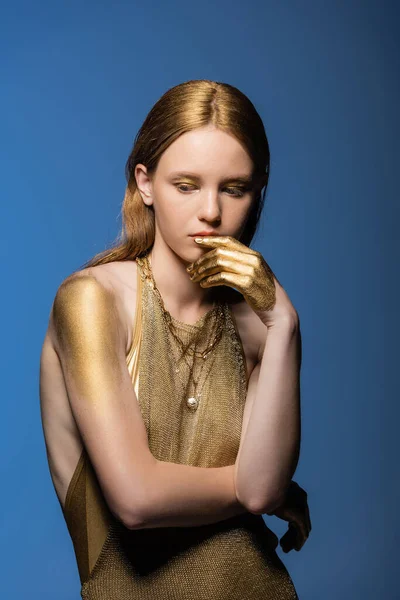 Молодая женщина с золотой краской на руках и плечах позирует изолированно на синий — стоковое фото