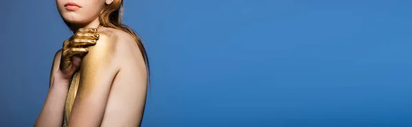 Обрезанный вид молодой модели с золотой краской на руке касаясь плеча изолированы на синий, баннер — Stock Photo