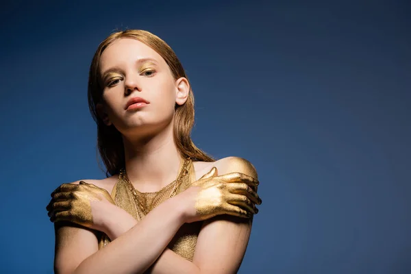 Hübsches Model mit Make-up und goldener Farbe auf den Händen, die vereinzelt auf blauem Grund in die Kamera schauen — Stockfoto