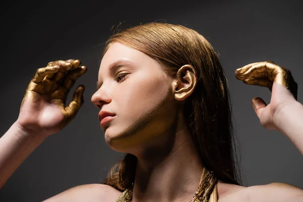Schönhaariges Model mit goldenen Händen, die vereinzelt auf grauem Grund wegschauen — Stockfoto