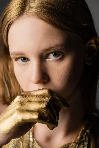 Retrato de mulher jovem com tinta dourada na mão olhando para a câmera isolada no cinza — Fotografia de Stock