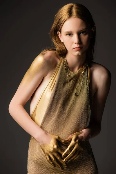 Frau in Kleid und goldener Farbe blickt in die Kamera auf grauem Hintergrund — Stockfoto