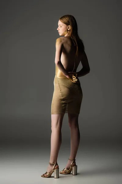 Pleine longueur de femme élégante en peinture dorée debout sur fond gris — Photo de stock
