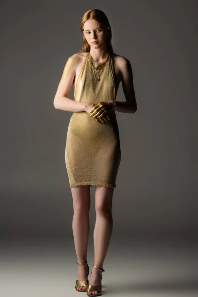 Full length of young woman in golden dress and paint looking away on grey background — Stock Photo