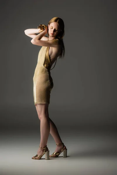 Volle Länge der Frau in Kleid und goldener Farbe auf Haar und Hände posieren auf grauem Hintergrund — Stockfoto