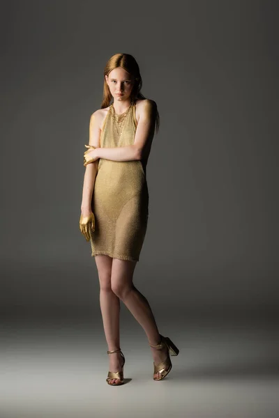 Trendige Frau in goldener Farbe und Kleid blickt in die Kamera auf grauem Hintergrund — Stockfoto