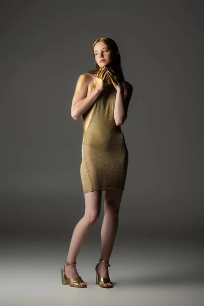 Pleine longueur de jeune modèle élégant en peinture dorée sur la peau debout sur fond gris — Photo de stock