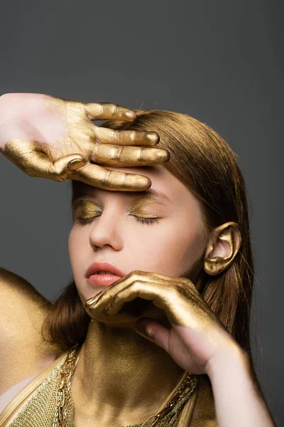Portrait of young woman with golden glitter on skin posing isolated on grey — Stock Photo