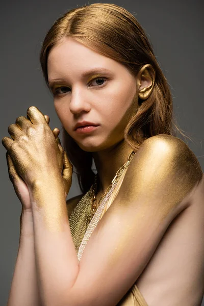 Portrait of fair haired woman with shiny golden paint on skin looking at camera isolated on grey — Stock Photo