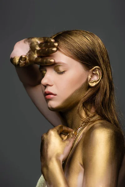 Mulher com brilho dourado na pele posando com olhos fechados isolados em cinza — Fotografia de Stock