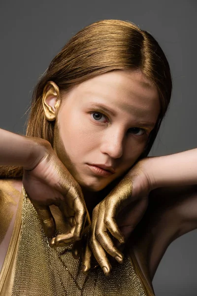 Porträt einer Frau mit goldenem Farbstoff auf Haar und Haut, die isoliert auf grau in die Kamera blickt — Stockfoto
